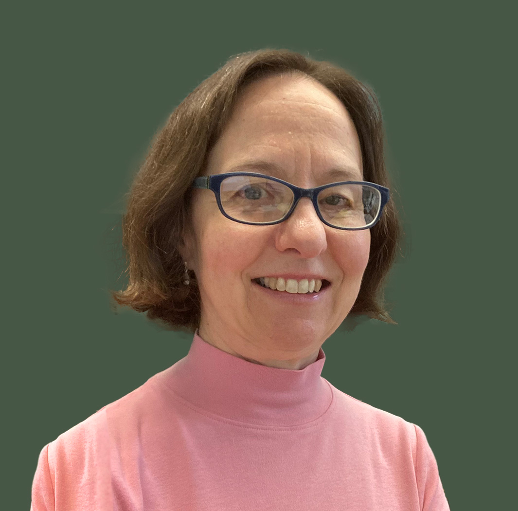 Bess Garrett with chin-length brown hair and blue glasses wearing a pink turtleneck shirt