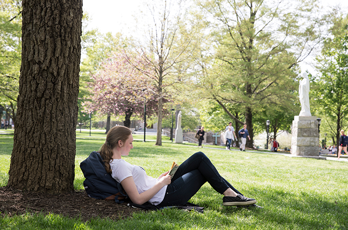 A student enjoys a book under the shade of one of the quad's many trees.