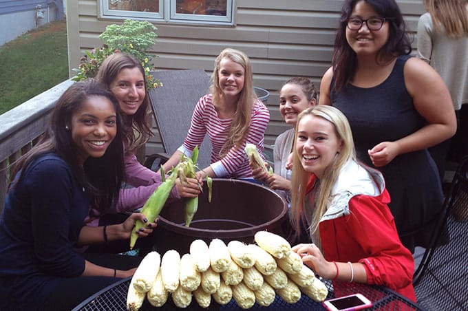 Students sitting around a table and shucking corn