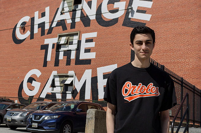 Andrew standing in front of a red brick wall with the words Change the Game written on it