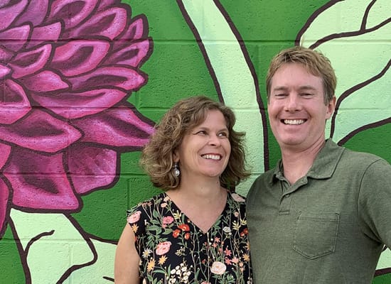 Ellen Frost and Eric Moller posing in front of a wall mural of a flower