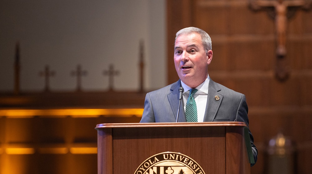 President Sawyer talking at a podium in the Loyola chapel - Press enter to play