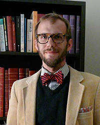 man in bow tie and tan jacket in front of a bookcase