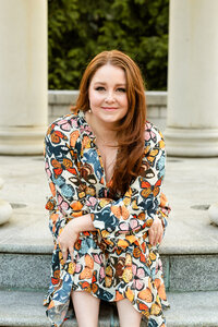 Lindsay Neutzling in a butterfly print dress, seated on a marble step and smiling at the camera.