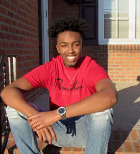 Daelin Cook, '23, smiling on the front porch steps of his home