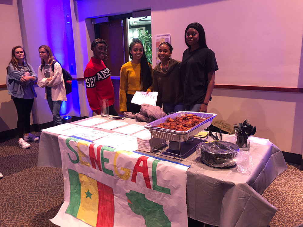 Students serving food at a table with a Senegal hand-made poster