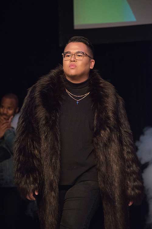 A male model in a big fur coat walking down the catwalk