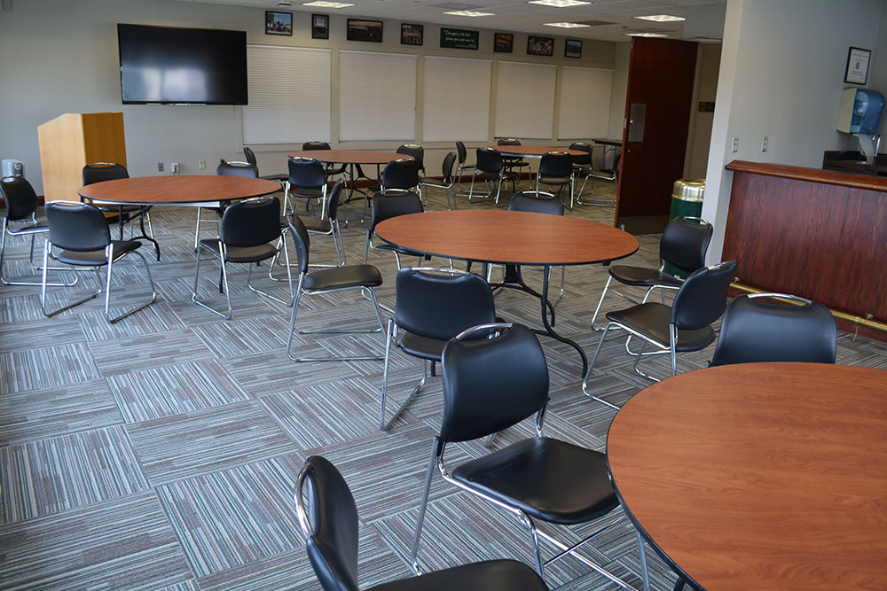 Round tables with chairs with a TV on the wall in the background, and windows that overlook Reitz Arena