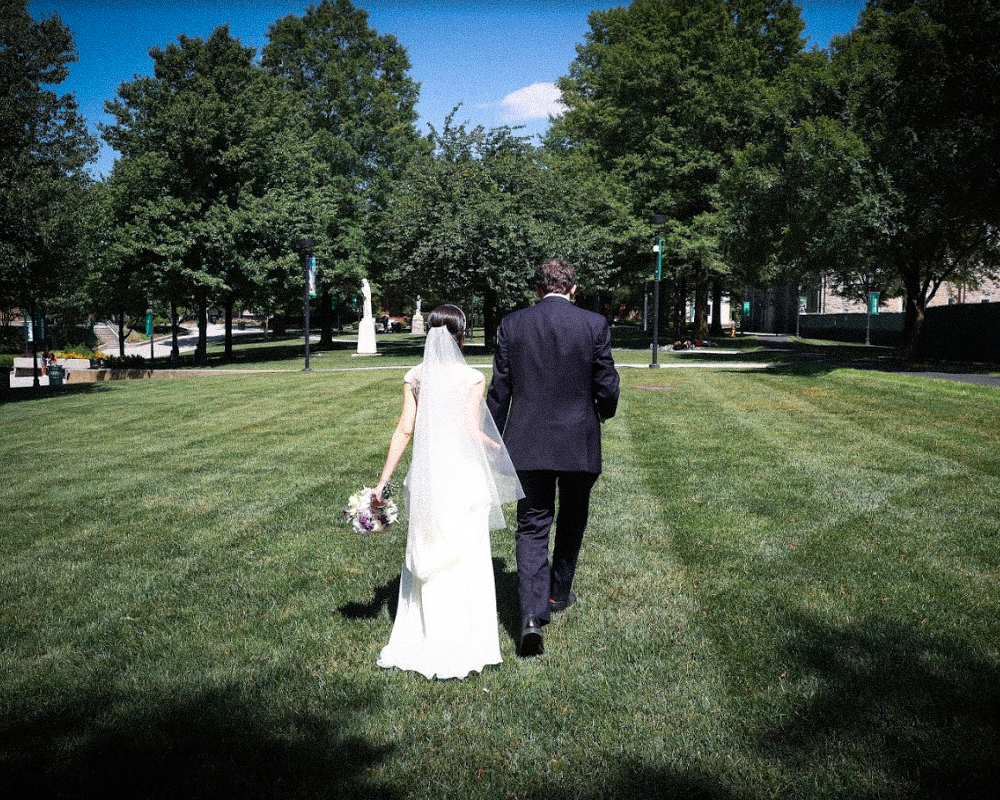 The backs of a recently married couple as they walk across Loyola's Quad near the Chapel