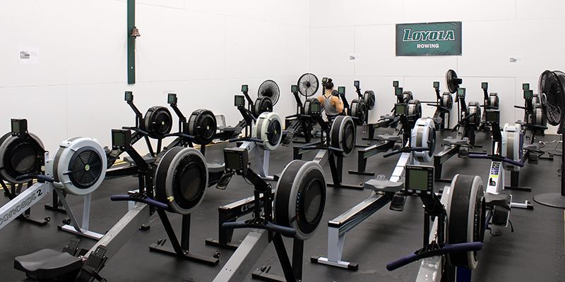 A large room with dozens of rowing machines and a student exercising on one of them