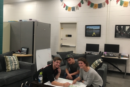 three students sit in basecamp around map
