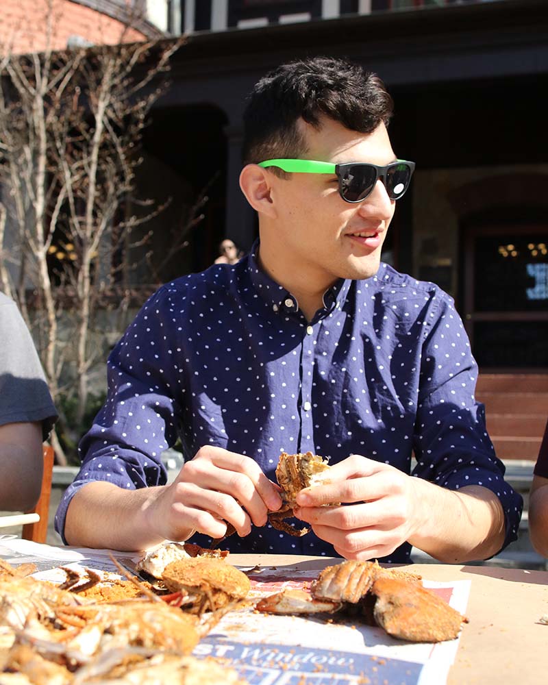 A male student wearing sunglasses enjoying a crab feast in front of the Humanities building