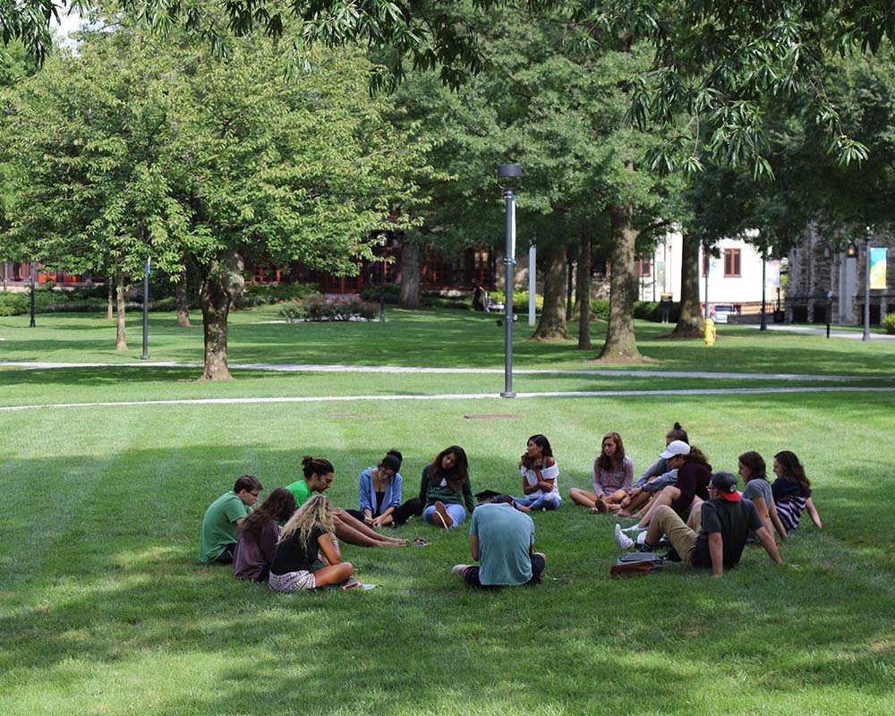A group of students sitting in a circle on Loyola's grassy and shaded academic Quad
