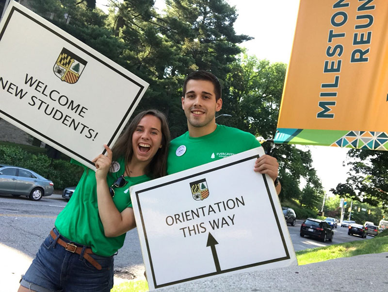 Two upperclassmen holding signs, smiling, and directing traffic during student move in