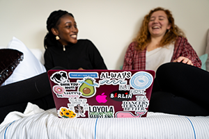 Two students in a dorm room laughing with a computer