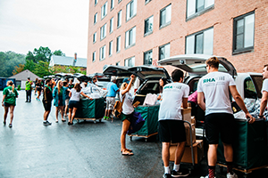Students helping students unpack cars parked outside of a residence hall