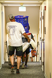 Parent carrying dorm belongings through a hallway