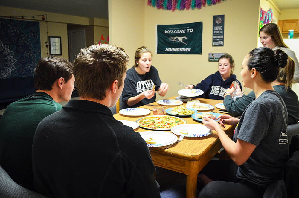 A group of sits around the table eating dinner in their dorm room