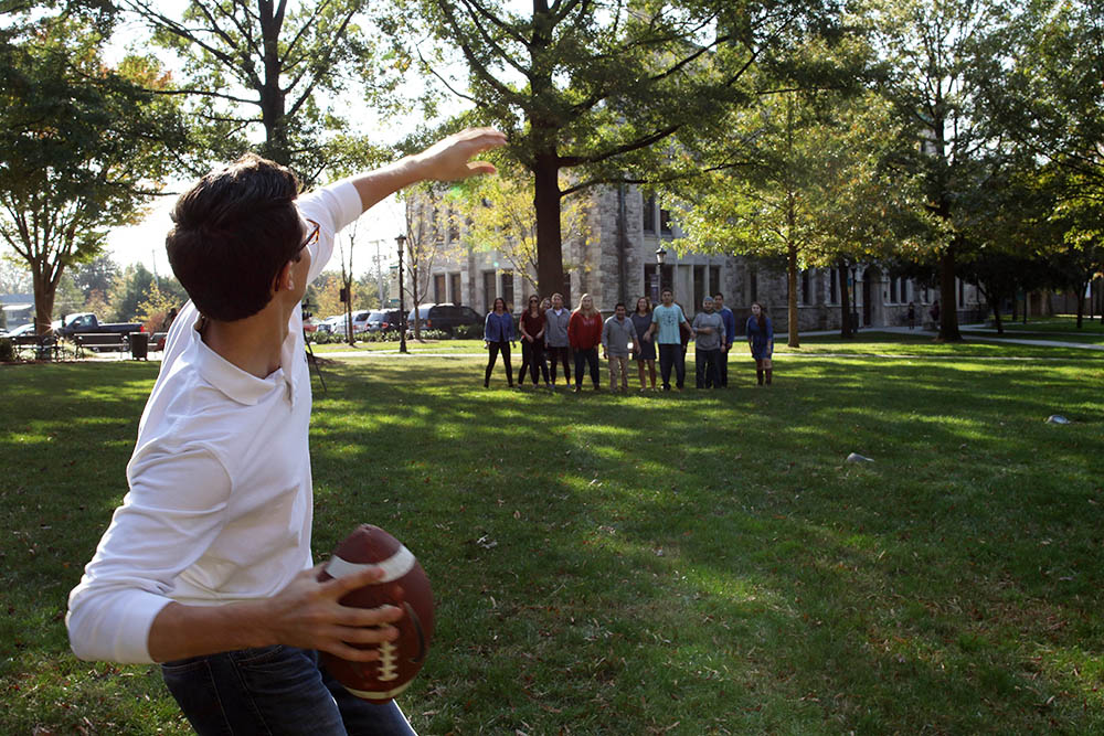 A student winds up to throw a football to a group of students on Loyola's quad