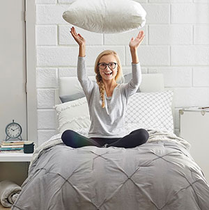 Person sitting on a bed throwing a pillow in the air