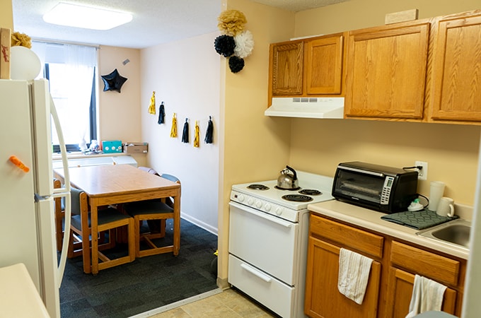 The interior of a dorm room kitchen with a dining table set in the connecting room