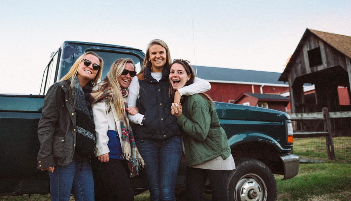 Students laughing and smiling in front of truck on a farm