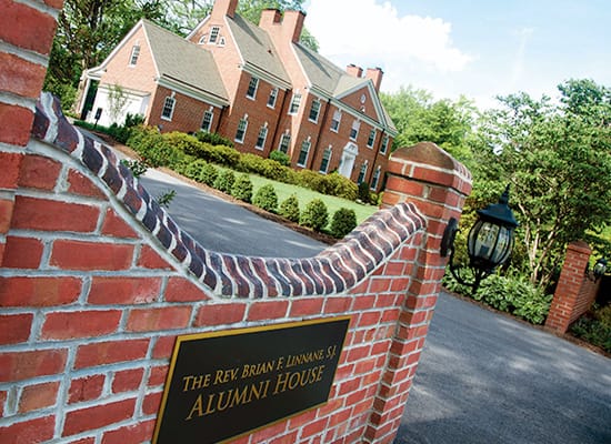A red brick wall with a sign reading The Rev. Brian F. Linnane Alumni House, and a red-bricked building in the background