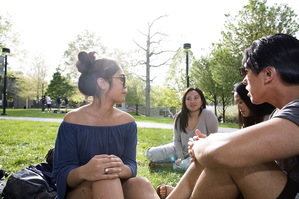 A group of students sitting on a blanket on the grass of the quad on a sunny day