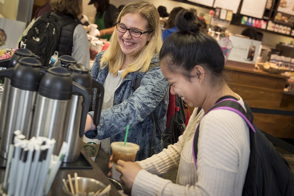 Two students chatting and laughing while filling their coffee cups in the student center