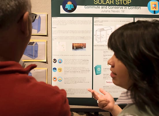 A student talks with a man in the foreground, while a poster for SolarStop can be seen in the background