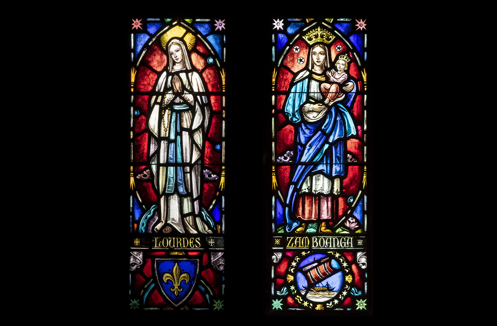 Two colorful stained glass panels of Our Lady of Lourdes and Our Lady of the Pillar