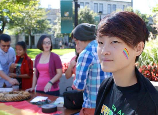 A student with a rainbow painted on her cheek with other students blurred in the background
