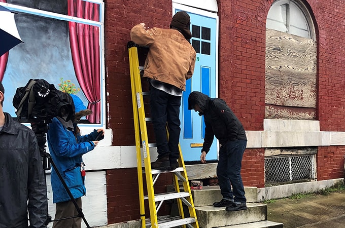 Two students installing a bright blue door on an abandoned rowhouse