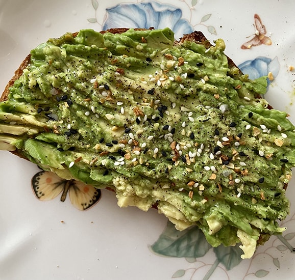 A slice of avocado toast sitting on a decorative plate