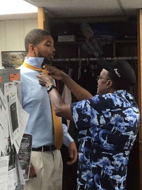 Volunteer helping tie a necktie on a member of the Govans community