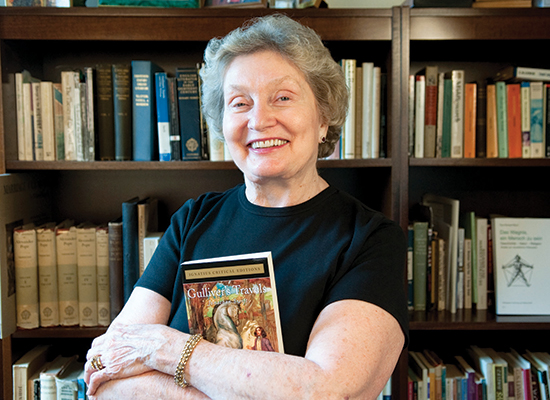 Carol Abromaitis holds a book with brown bookshelves behind her.