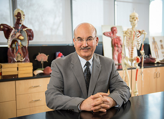 Bahram sitting in a classroom surrounded by anatomical models.
