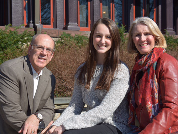 Meredith sitting with her parents in front of the humanities manor.