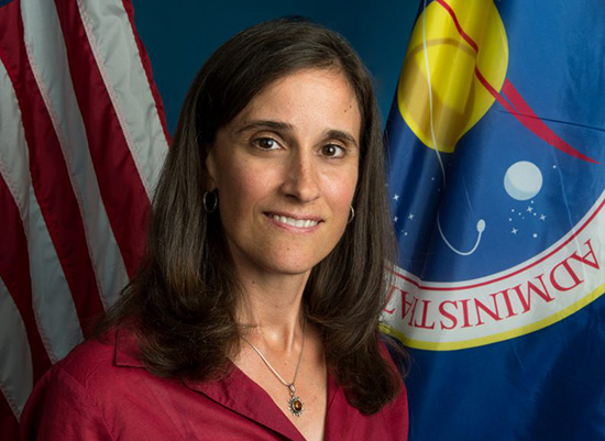 Professional photo of Lisa Mazzuca who is flanked by flags of the USA and NASA.