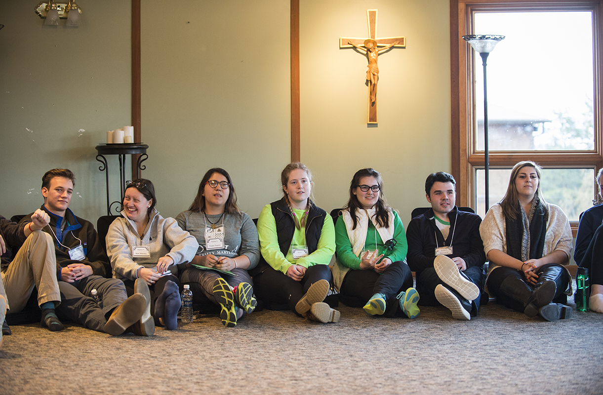 Students sit against the wall with a crucifix above them.