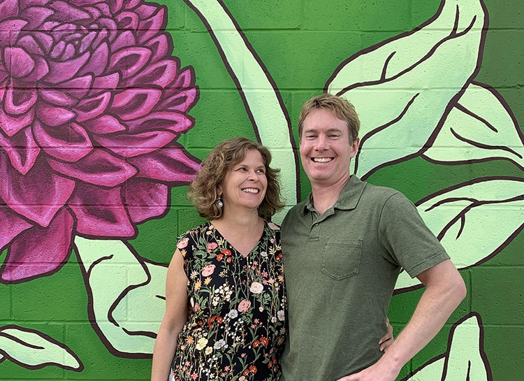 Ellen Frost and Eric Moller posing in front of a wall mural of a flower