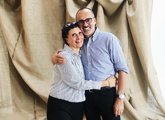 Mary Gamberdella and Brian Rogers standing together with large, beige fabric draped behind them.