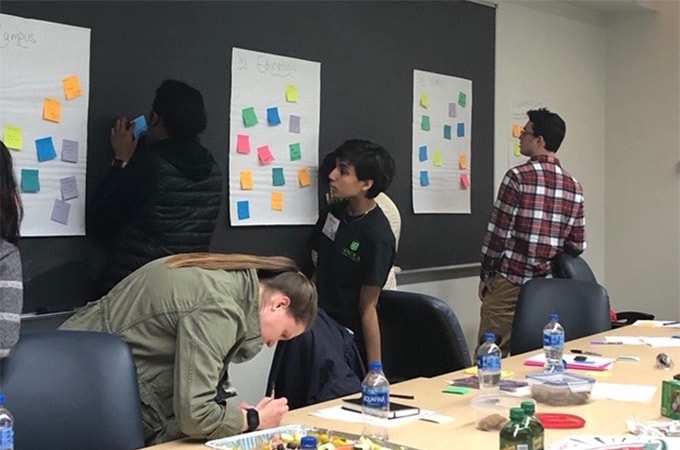 A group of students in the Social Impact Fellowship program brainstorm ideas to write down and categorize on a wall