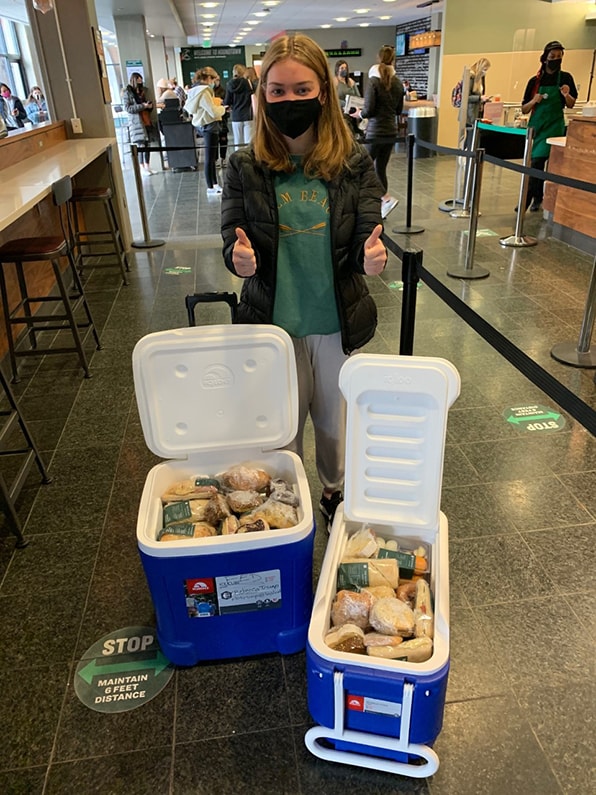 Loyola student, Jess Ludwig, posing with coolers full of food that F.E.D. has recovered