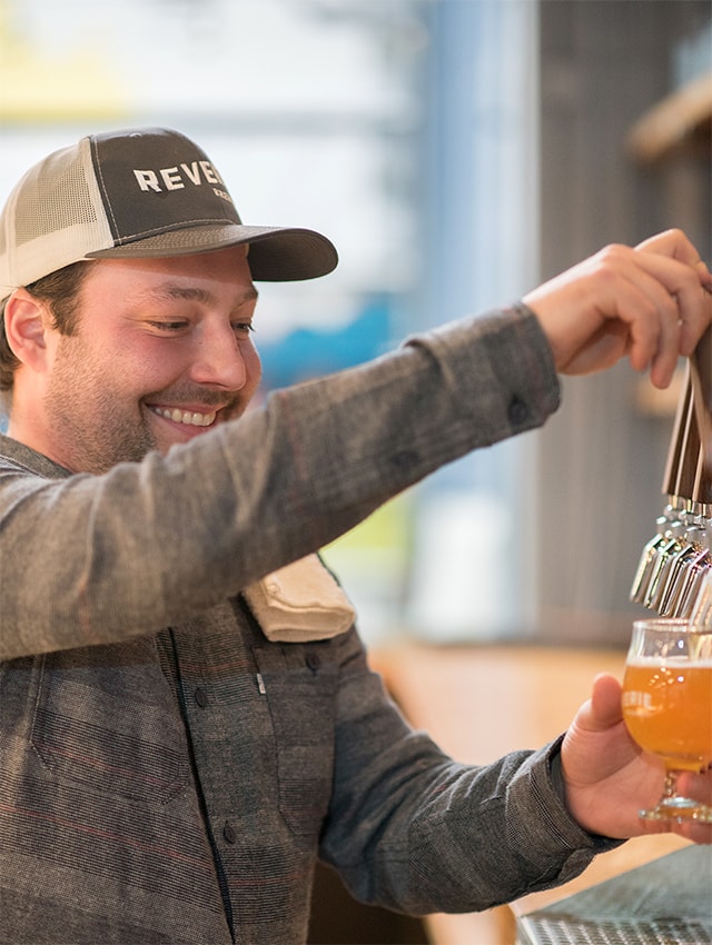 An employee pours beer from a tap with a smile
