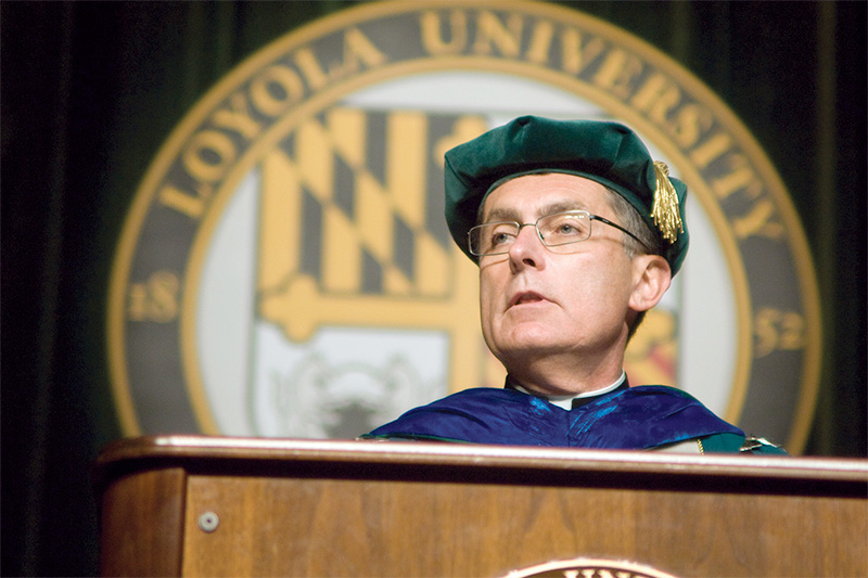Father Linnane speaking at a podium wearing academic robes