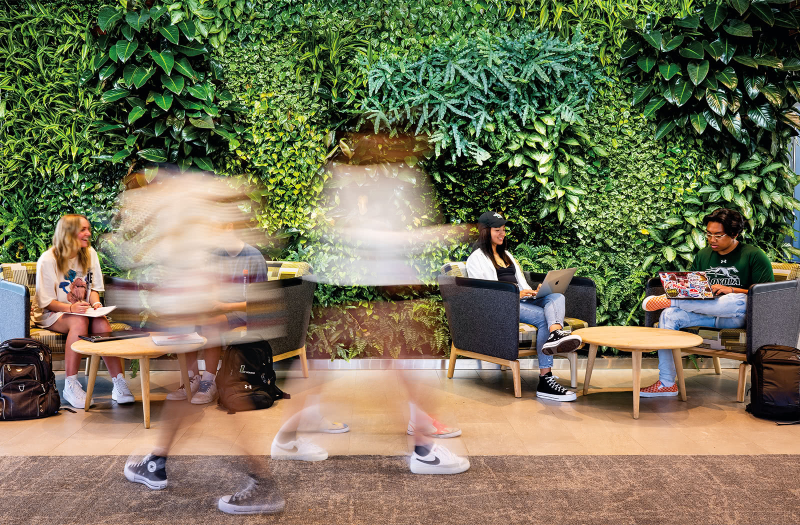 Several students sitting at tables in front of the living green wall inside the Fernandez Center