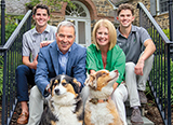 The Sawyer family pose for a photo with their two dogs sitting on the stairs outside their home