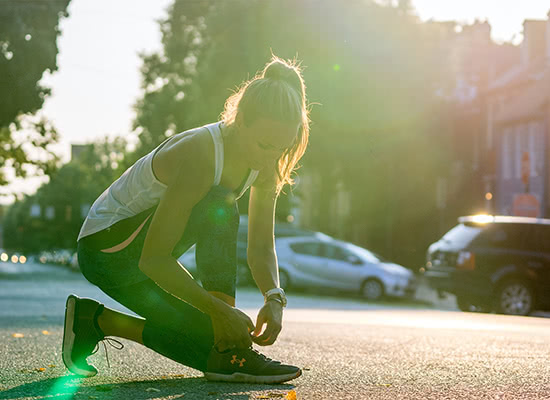 Sandra Gallagher-Mohler kneels down to tie her shoe during a run with the sun setting in the background