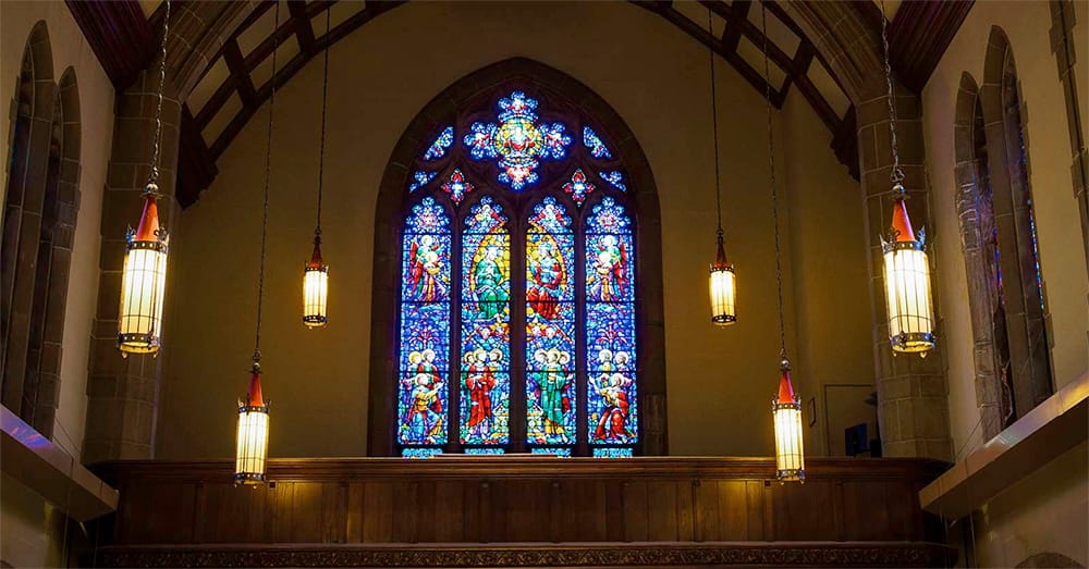 Stained glass and hanging lanterns light up the interior of the Alumni Memorial Chapel